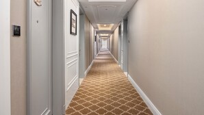 Un pasillo de hotel con alfombra estampada, paredes blancas y puertas con números de habitación.