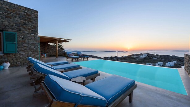 A poolside area with lounge chairs and a stone building. - My Rental Homes - Villa Joy with sea view, pool equipped with sunbeds and patio (Mykonos)