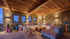 A cozy interior with a stone wall, wooden ceiling, and a sofa set. - My Rental Homes - Villa Joy with sea view, pool equipped with sunbeds and patio (Mykonos)