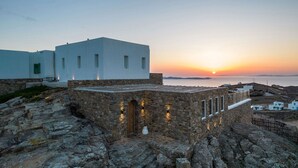 A modern white building with stone walls and a stone staircase leading to a wooden door. - My Rental Homes - Villa Joy with sea view, pool equipped with sunbeds and patio (Mykonos)