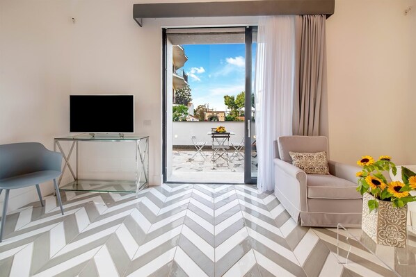 Een moderne woonkamer met een flatscreen televisie, een bank, een glazen salontafel en een eethoek met een tafel en stoelen.