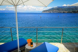 A balcony with a view of the sea, a table with a bottle and glasses, and blue cushioned chairs. - Villa Marina Grande with jacuzzi - My Rental Homes (Sorrento)