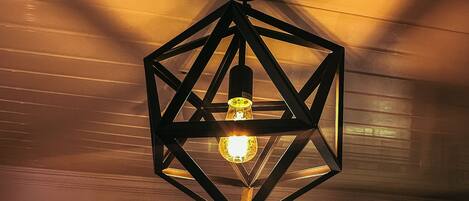 Una lámpara colgante hexagonal con bombilla visible, suspendida del techo con vigas al descubierto.