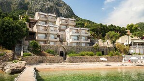 Un hôtel à plusieurs étages doté de balcons, d’un mur en pierre et d’un espace de plage avec des parasols.