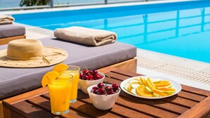 Un coin petit-déjeuner installé au bord de la piscine, avec une table, des boissons et des fruits.
