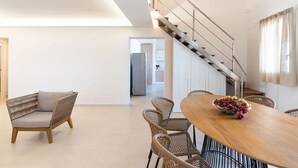 Un'ampia zona giorno con un tavolo da pranzo in legno, sedie in vimini e una scala che conduce a un piano superiore.