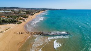 Una vista aerea di una zona costiera con spiaggia sabbiosa, acque blu cristalline e una città all'orizzonte.