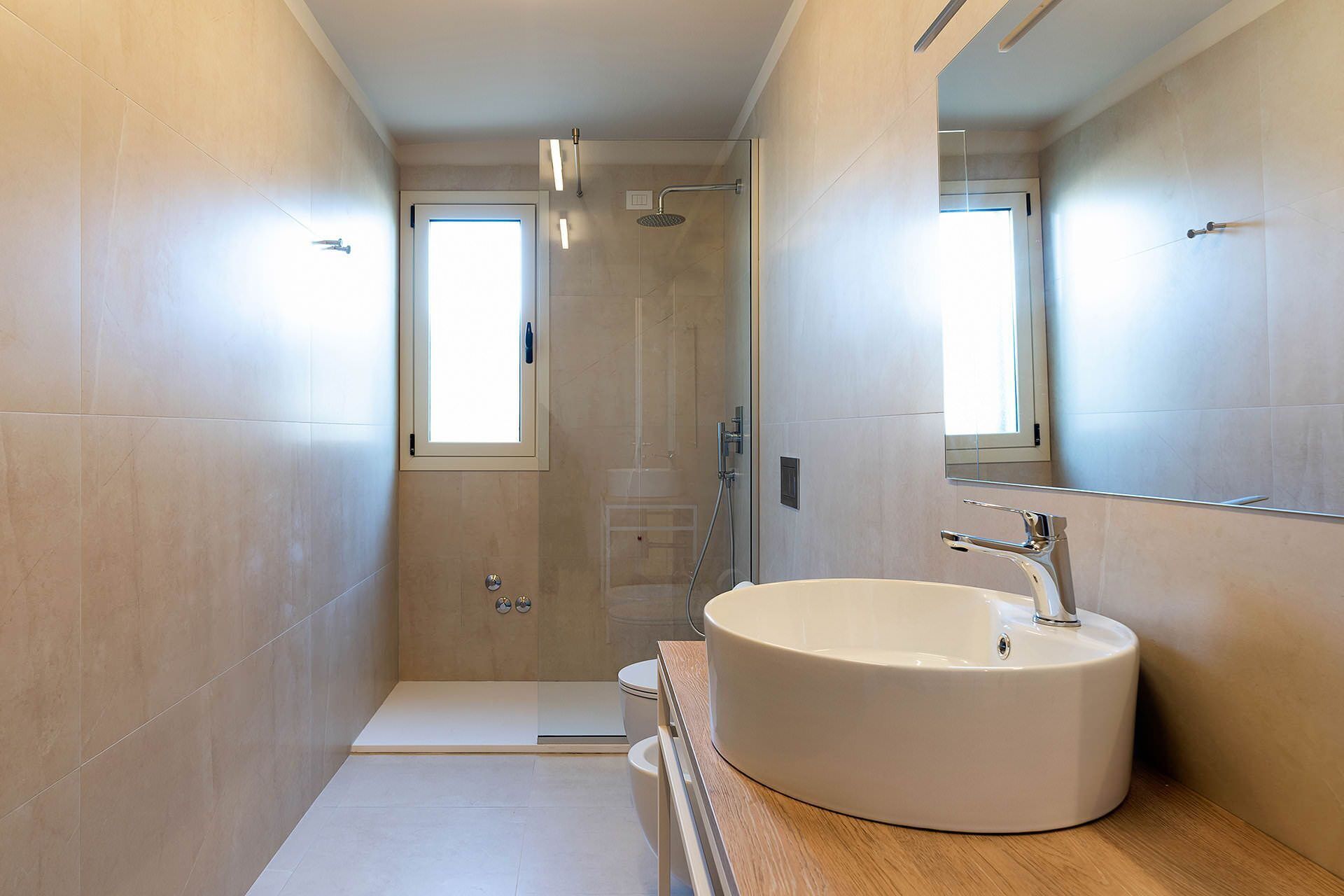 A modern bathroom with a large mirror, a round sink, and a shower enclosure.