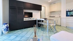 Una cocina moderna con armarios blancos, un comedor con mesa y sillas, y un jarrón grande en el suelo.