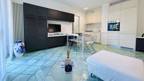Una cocina moderna con armarios oscuros, un comedor con mesa y sillas, y un refrigerador blanco.