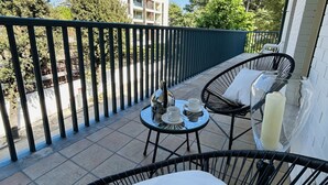 Un balcón con una mesa dispuesta para tomar té, dos sillas y vistas a un edificio y árboles.