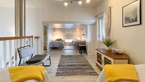 Una camera moderna e luminosa con un letto, una panca, un tavolino e un termosifone. Si vede una finestra con tende e una pianta sul tavolo.