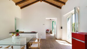 Una cocina moderna con una mesa de vidrio, sillas de madera, un refrigerador rojo y vistas al jardín a través de la puerta abierta.