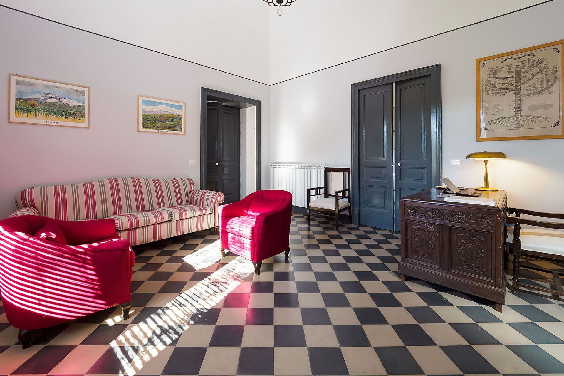Une pièce avec un sol à carreaux, un canapé à rayures, un fauteuil rouge, un meuble en bois et deux portes.