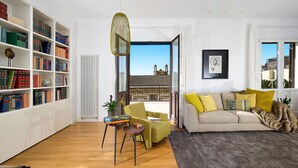 Un salon comprenant une bibliothèque, un canapé, un fauteuil, une table et une vue sur l’extérieur.
