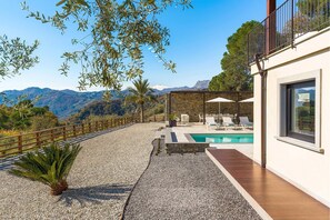 A modern outdoor pool area with a view of mountains, a pergola with umbrellas, and a stone wall. - Villa Zafferano with pool - My Rental Homes (Savoca)