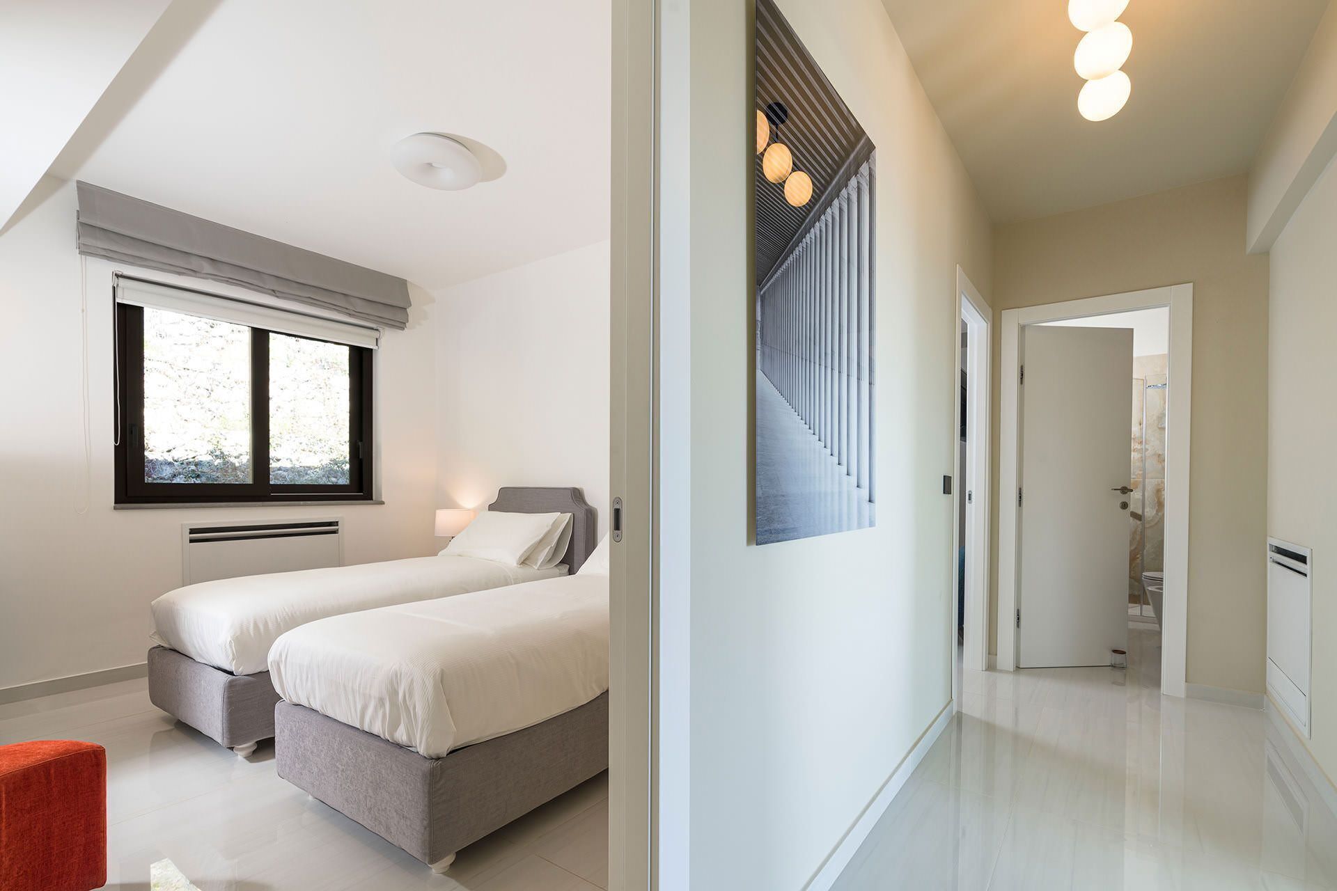 Et moderne hotelværelse med to senge, et stort vindue og en gang der fører til et badeværelse.
