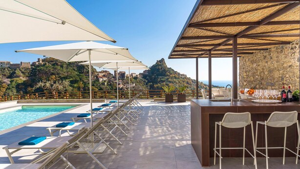 Zona de piscina con sillones de descanso, sombrillas y un bar con asientos.