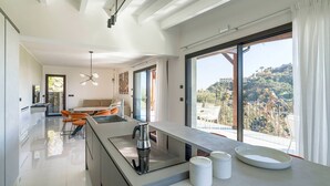 Cocina moderna con una isla grande, un comedor con sillas naranjas y vistas a un paisaje montañoso a través de amplios ventanales.