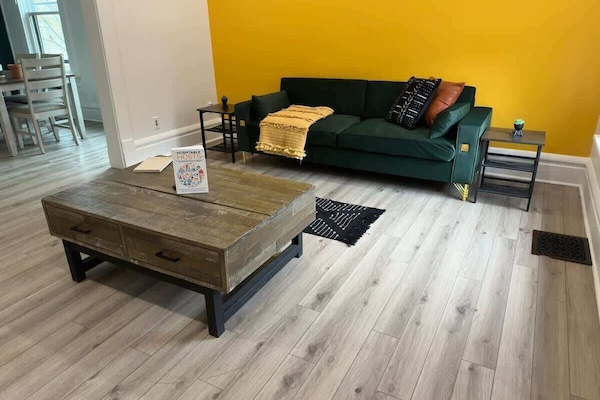 "& Unwind in style in our modern Jungle House living room in Columbus! Our vibrant orange tufted sofa, cozy yellow throw blanket, and chic cowhide rug create the perfect space to relax. & Our plants are looking forward to hosting you soon Book y