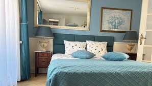 A bedroom with a bed, two bedside tables, a nightstand, a mirror, and a wall-mounted lamp.