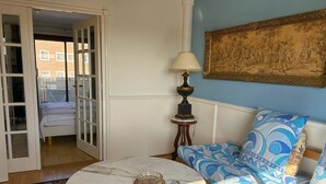 A room with a bed, a round marble table with a glass bowl, a lamp, and a patterned sofa.