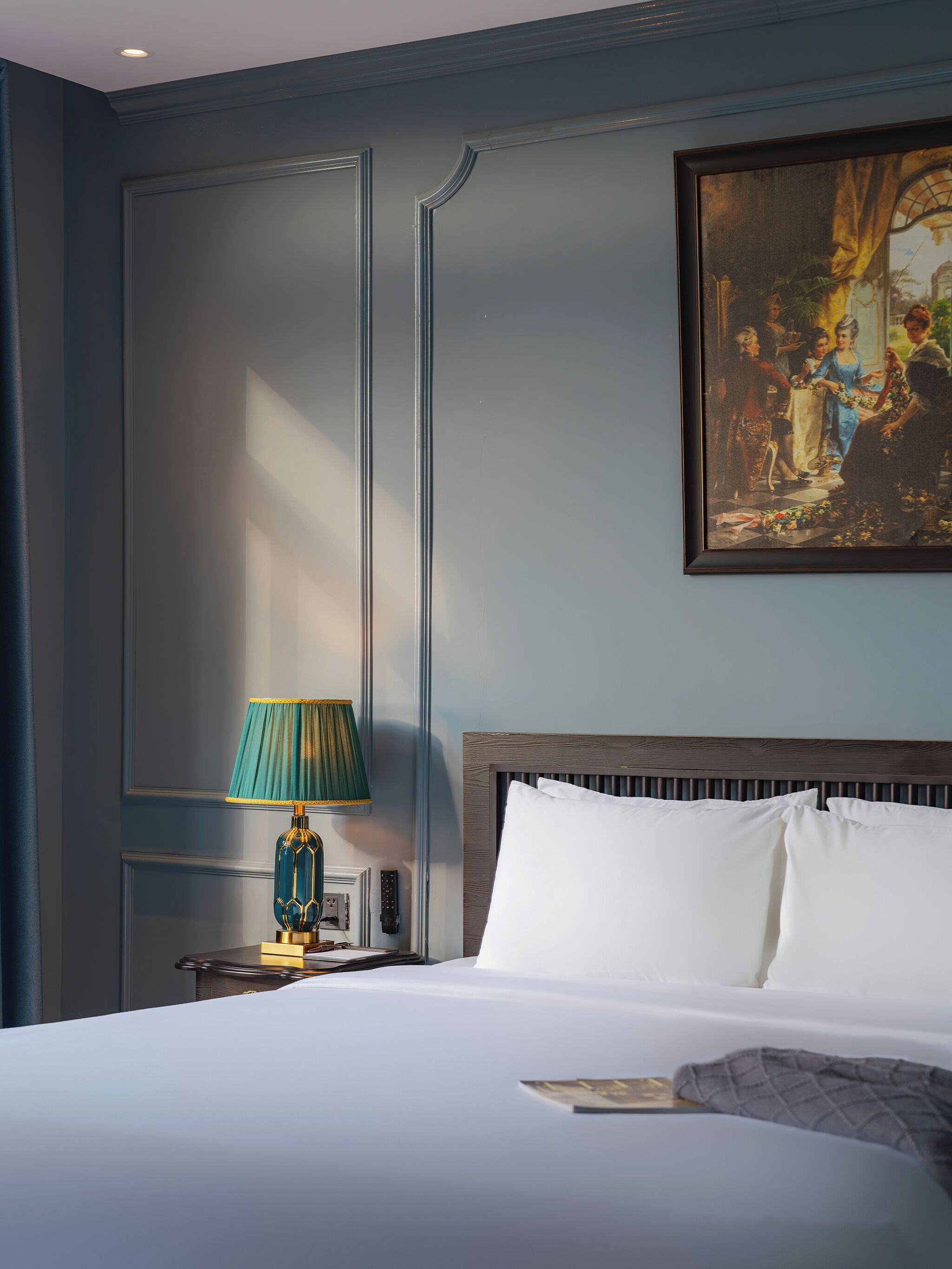 A hotel room with a large bed, a nightstand with a lamp, and a painting on the wall.