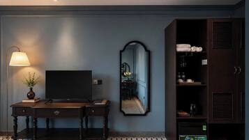 A hotel room with a dark wooden desk, a flat-screen TV, a mirror, and a wardrobe with shelves.