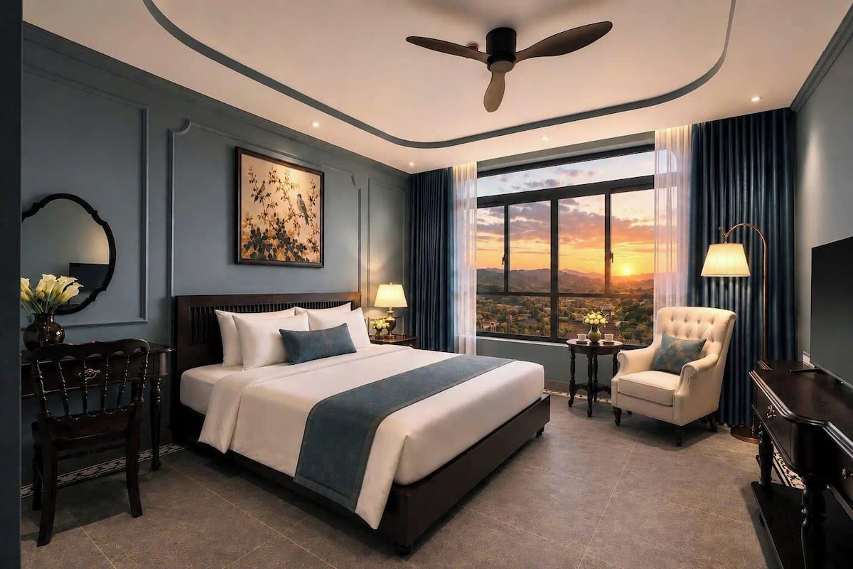 A hotel room with a large bed, a desk, a chair, a TV, and a view of the sunset through the window.