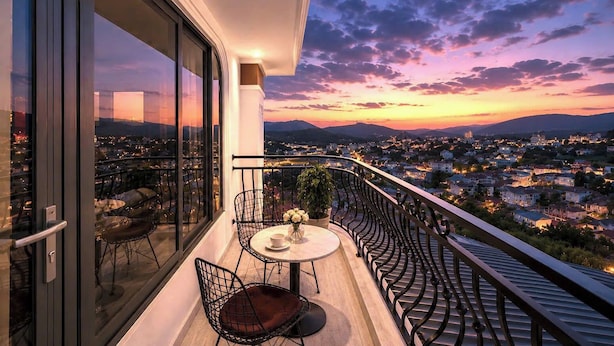 Un balcon avec une table et des chaises, offrant une vue sur le paysage urbain au coucher du soleil.