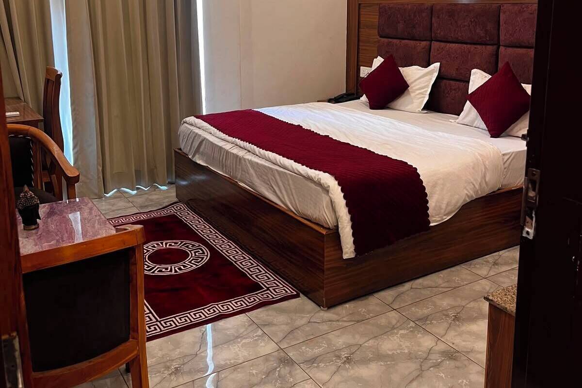 A bedroom with a bed, a ceiling fan, an air conditioning unit, a wooden chair, and a patterned rug.