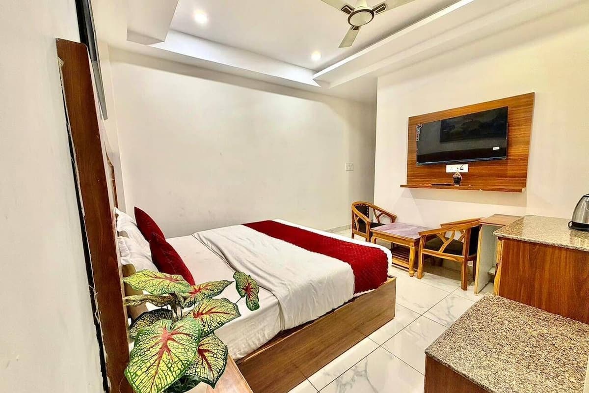 A bedroom with a bed, a TV mounted on the wall, a desk, and a chair.
