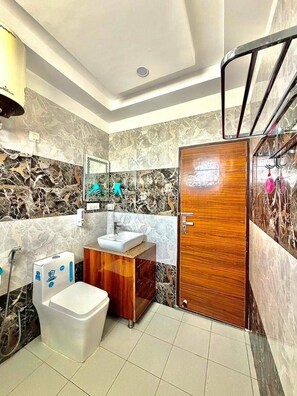 A bathroom with a wooden door, a white sink, a toilet, and a mirror. - Shree ji Retreat - A Boutique Stay (Rishikesh)