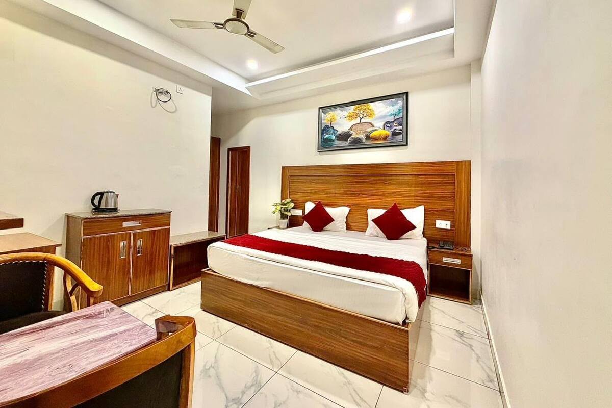 A hotel room with a bed, wooden headboard, a ceiling fan, a painting, a desk with a chair, and a cabinet.