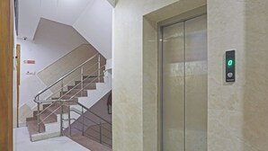 An elevator with a digital display, a staircase with metal railings, and a tiled floor. - HOTEL STAR LITE (New Delhi)