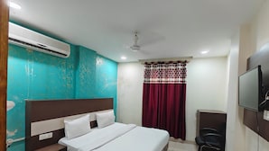 A hotel room with a bed, bedside table, air conditioning unit, ceiling fan, TV, and a red curtain. - HOTEL STAR LITE (New Delhi)