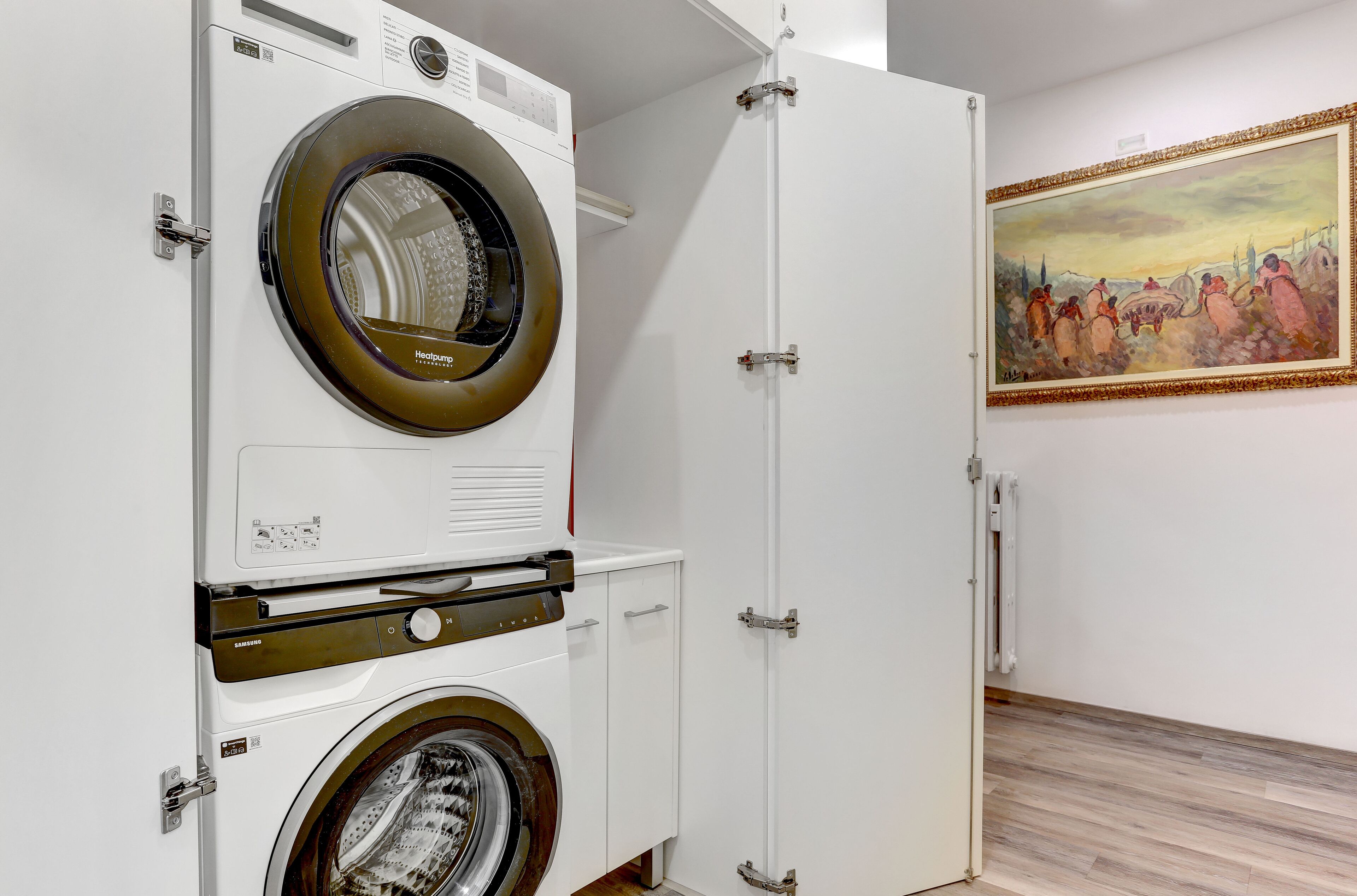 Une buanderie avec des machines à laver et des sèche-linge superposés, une porte et un tableau accroché au mur.