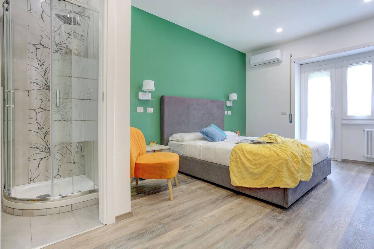 Ein modernes Schlafzimmer mit einer Glasdusche, einem Bett mit gelber Decke und einer grünen Akzentwand.