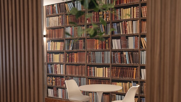 Een bibliotheek met boekenkasten en twee witte stoelen rond een tafeltje.