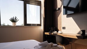 Een hotelkamer met een bed, een bureau met een koffiezetapparaat, een kop, een schoteltje, een potplant en een televisie aan de muur.