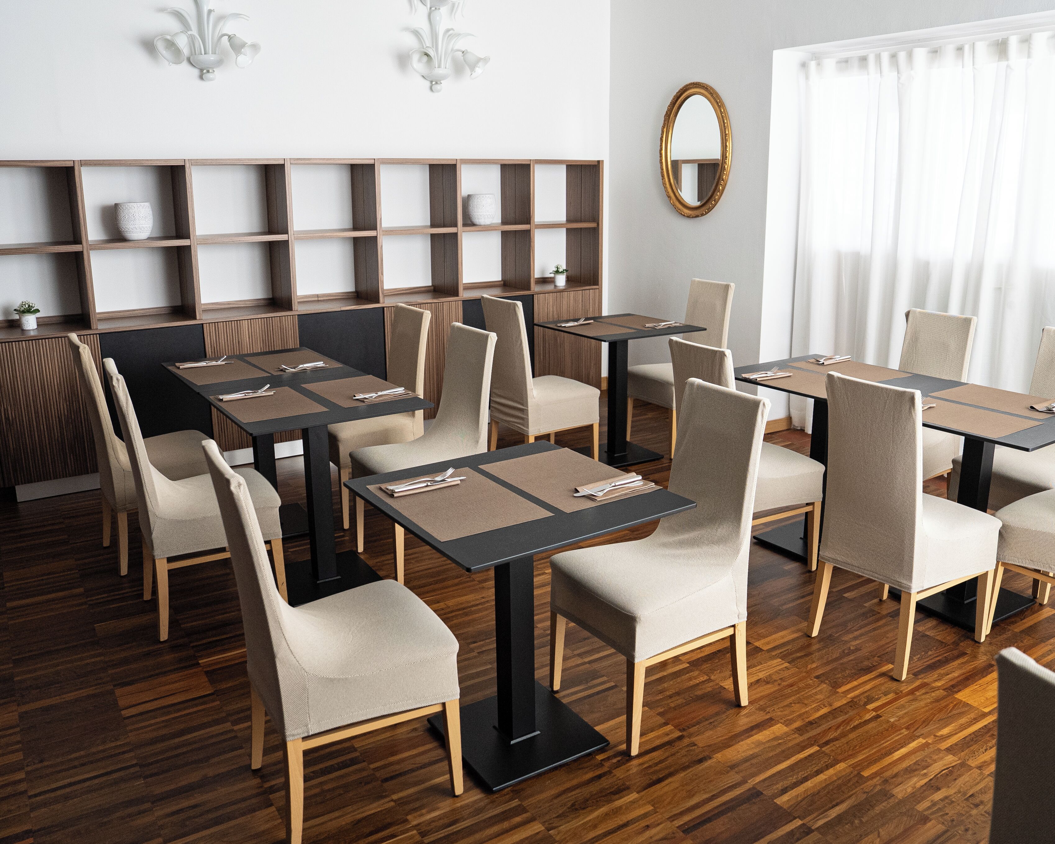 A modern dining area with wooden flooring, beige upholstered chairs, and black tables.
