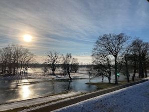 A winter landscape with a frozen river, bare trees, and a clear sky. - Landhaus Elbeflair Apartment GmbH (Lenzerwische)