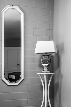 A corner with a white-framed mirror and a white table lamp with a white lampshade against a brick wall. - Landhaus Elbeflair Apartment GmbH (Lenzerwische)