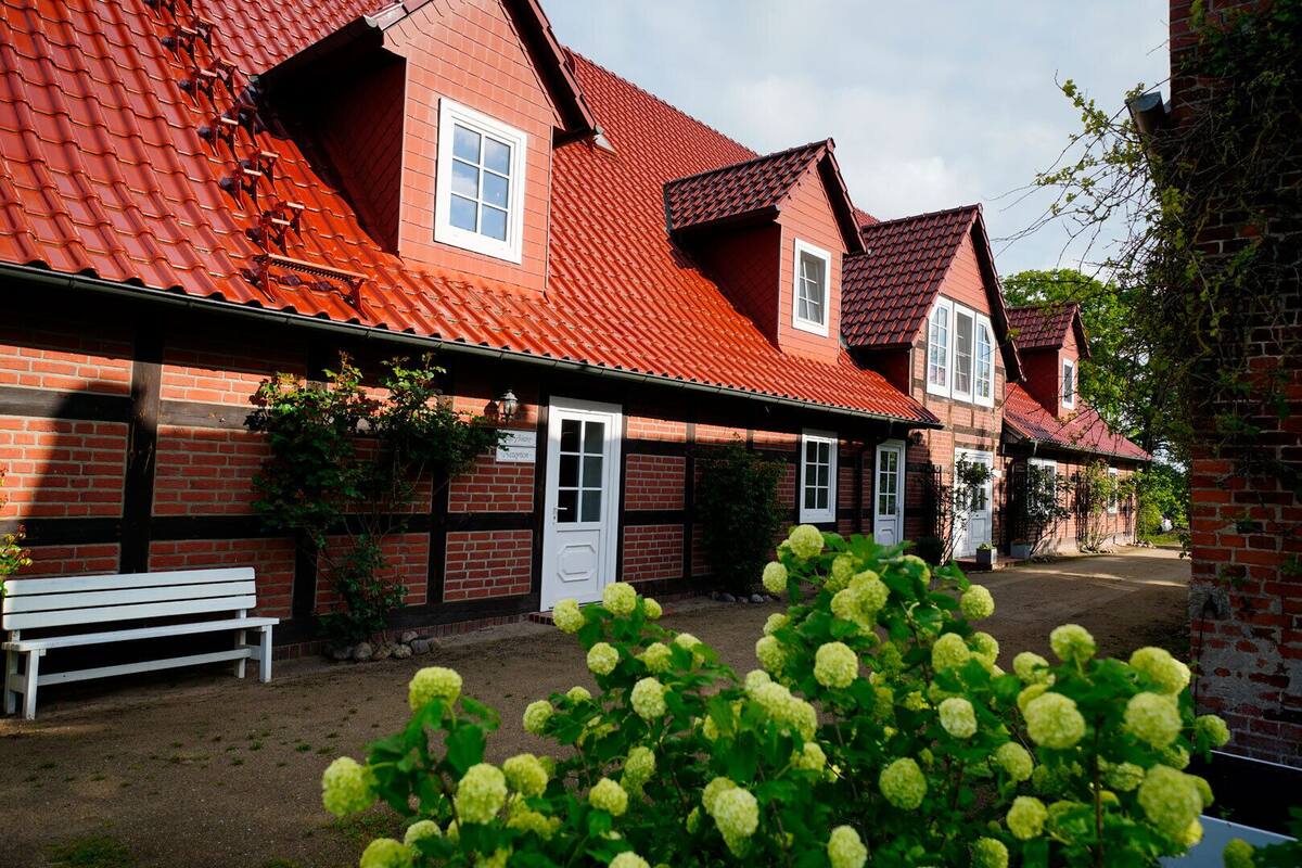 A row of red-roofed houses with brick walls, a bench, and green plants in the foreground.