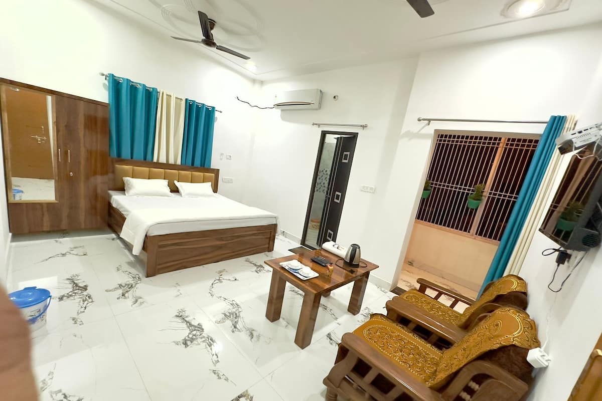 A hotel room with a bed, a wooden table, a sofa, a wardrobe, a ceiling fan, and a window with curtains.