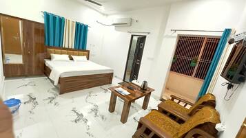 A hotel room with a bed, a wooden table, a sofa, a wardrobe, a ceiling fan, and a window with curtains.