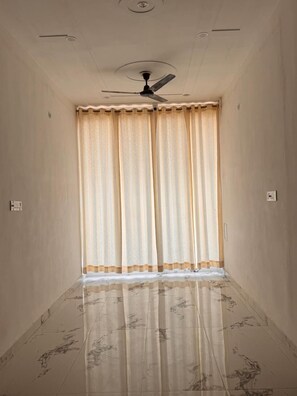A room with a ceiling fan, a window with curtains, and a tiled floor. - Ramalayam (Faizabad)