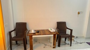 A room with a wooden table and two chairs, a small table with a teapot and cups, and a power outlet on the wall. - Ramalayam (Faizabad)