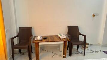 A room with a wooden table and two chairs, a small table with a teapot and cups, and a power outlet on the wall.