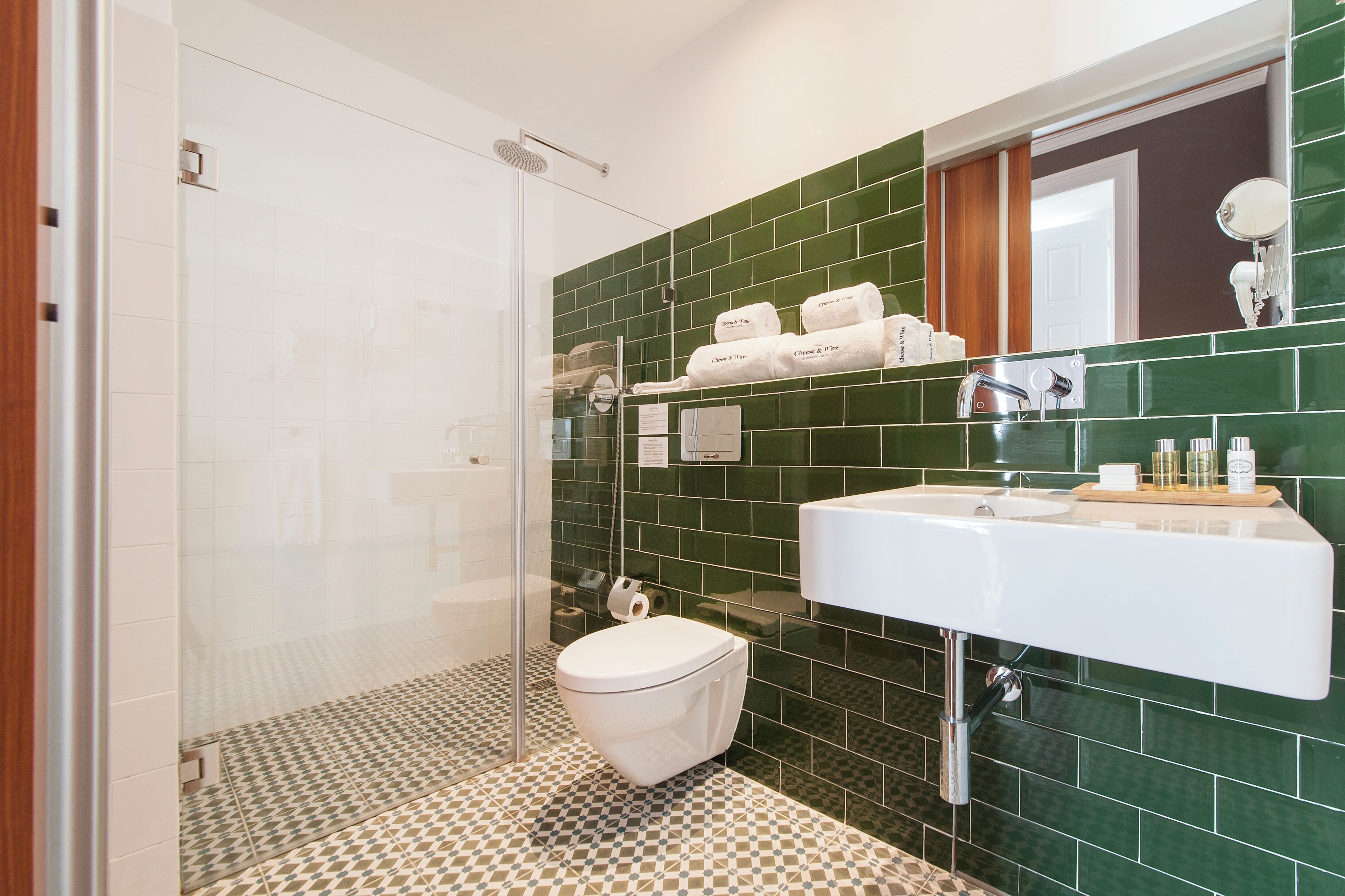 A bathroom with a shower, toilet, and sink, featuring green tiles and a patterned floor.